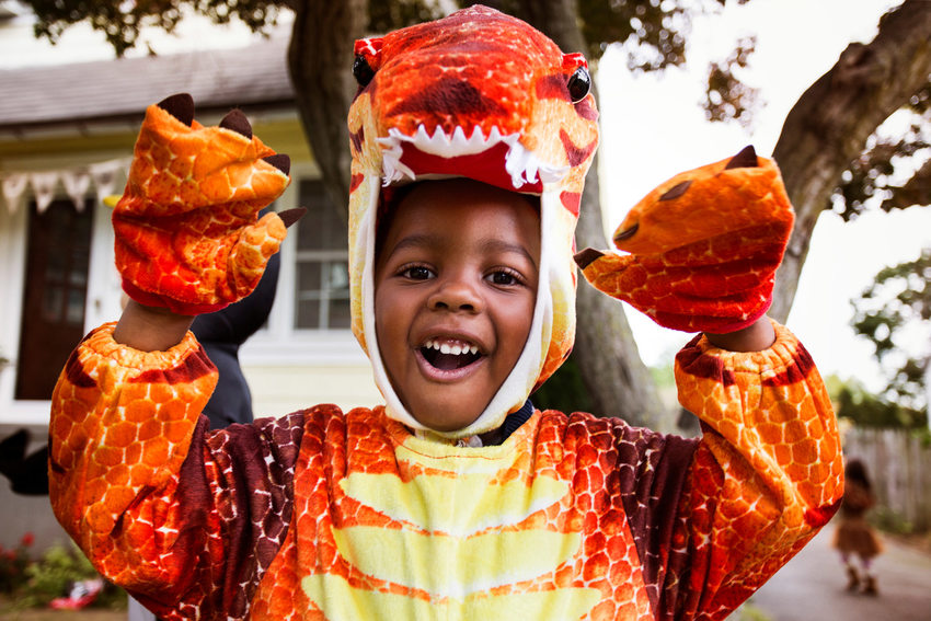 A child in a dragon costume raises his arms and makes a face for the camera
