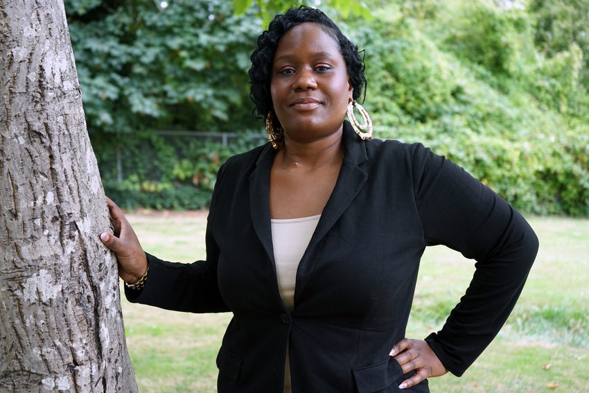 Woman in a black blazer posing next to a tree in a park. 