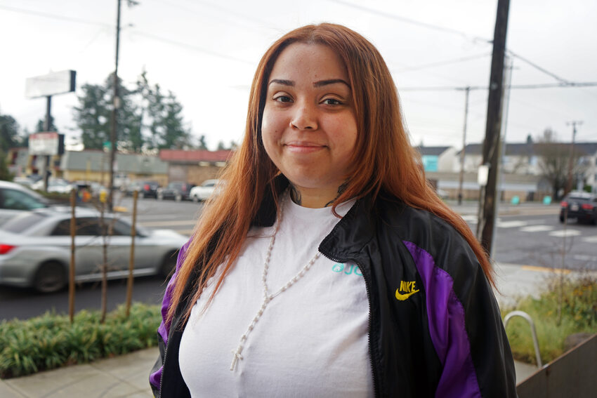 Woman with long red hair and Nike jacket with street in background.