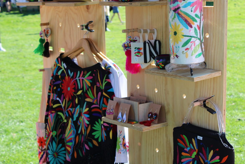A wooden display with colorfully embroidered clothing and accessories on it for sale at a vendor's booth