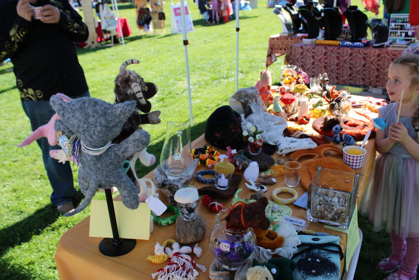 A child wearing a colorful dress stands next to a vendor booth filled with stuffed animals and crafts