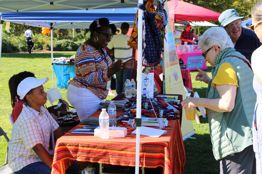A group of people standing at a vendor's colorful booth at the Holly Park Multicultural Fair in October 2023