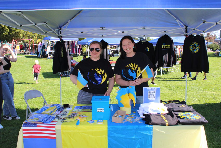 Two women standing at a table holding Ukrainian flags at the Holly Park Multicultural Fair in October 2023