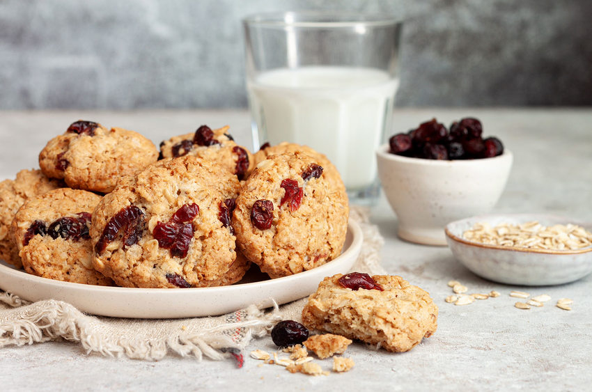 cookies and crumbs on a plate and spilling over onto a grey countertop, bowls of cranberries and oats are in the background