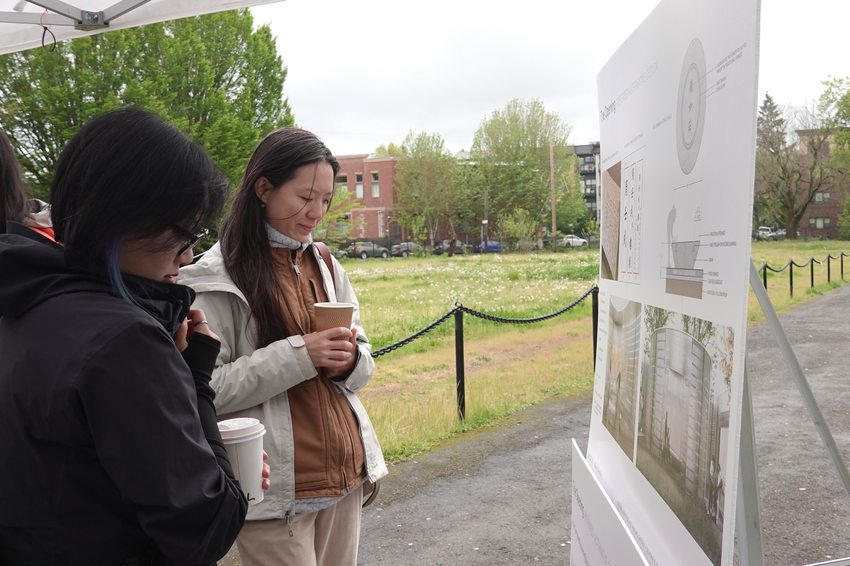 two women stand outdoors looking at informational posters about altar design