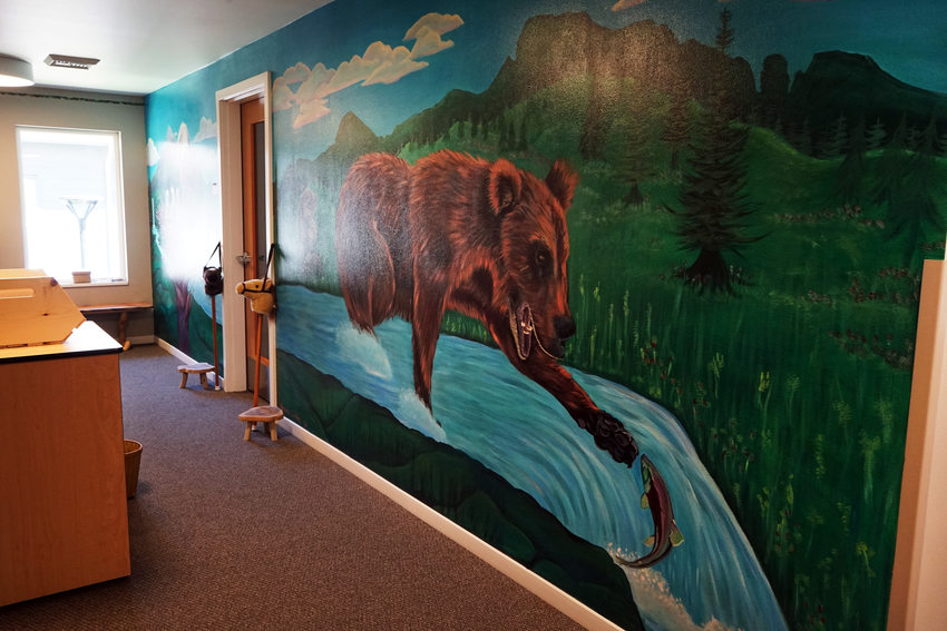 Large mural of a bear catching a salmon, on the wall of a hallway like space.