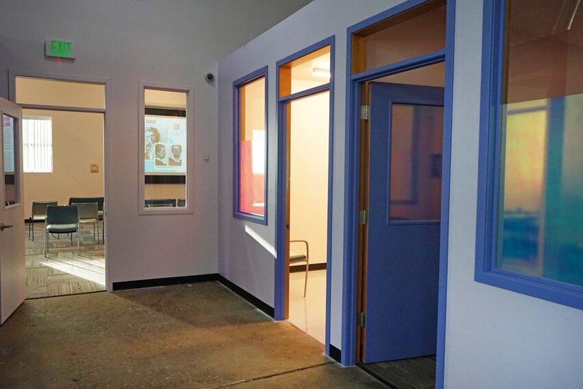 Office hallway with purple and lavender walls, leading to a large, light-filled room.