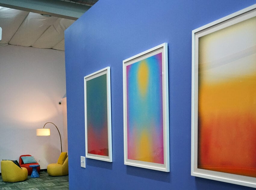 Framed art on a bright purple wall with seating in the background.