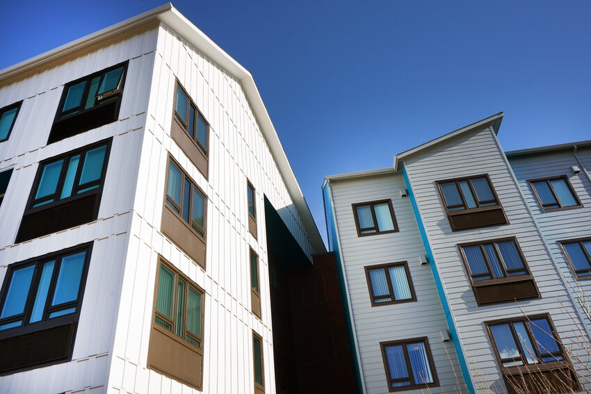 Looking up at a multi-story apartment building with white siding and wood accents.