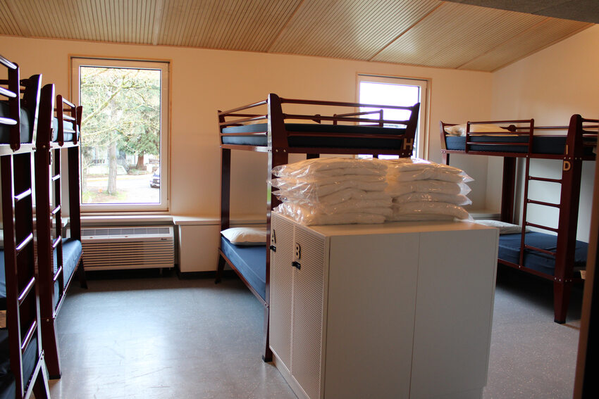 Group sleeping room with wood frame bunk beds and stacks of sheets