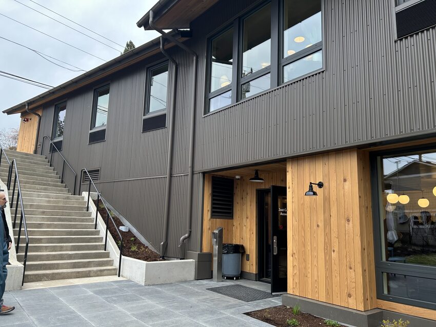 Entryway to two story building with grey and unfinished wood siding. 