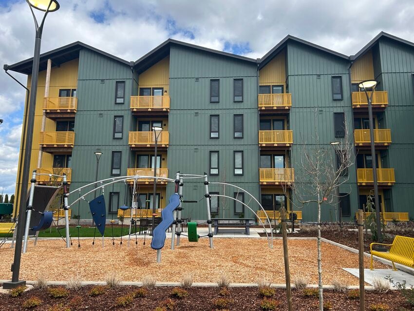 Four story apartment building with green siding and yellow accents. A playground is in the foreground.