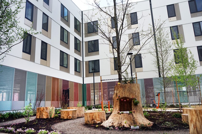 Apartment building courtyard with landscaping and stump seating and young trees.