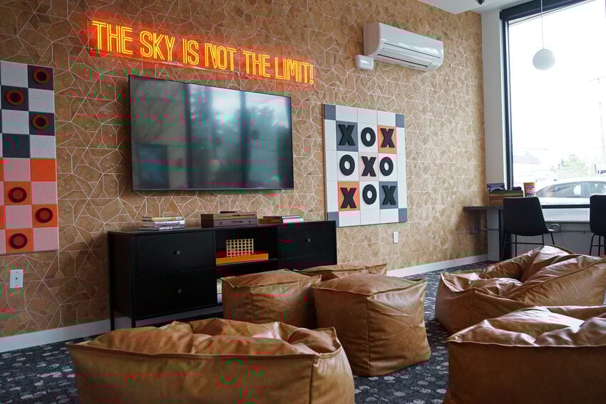 Lounge with comfy leather chairs and TV, plus a neon sign that reads, the sky is not the limit.