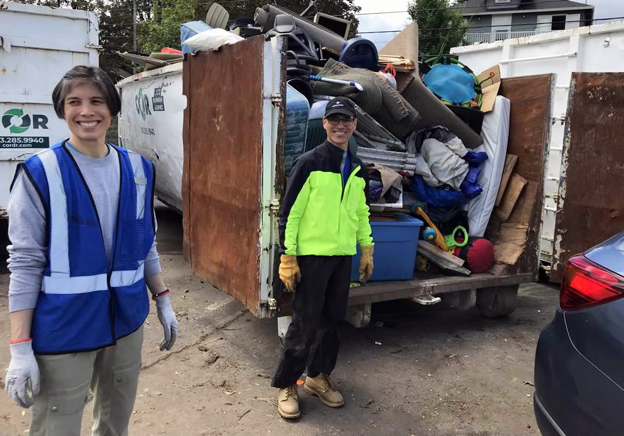 An image of two people in front of a trailer full of trash