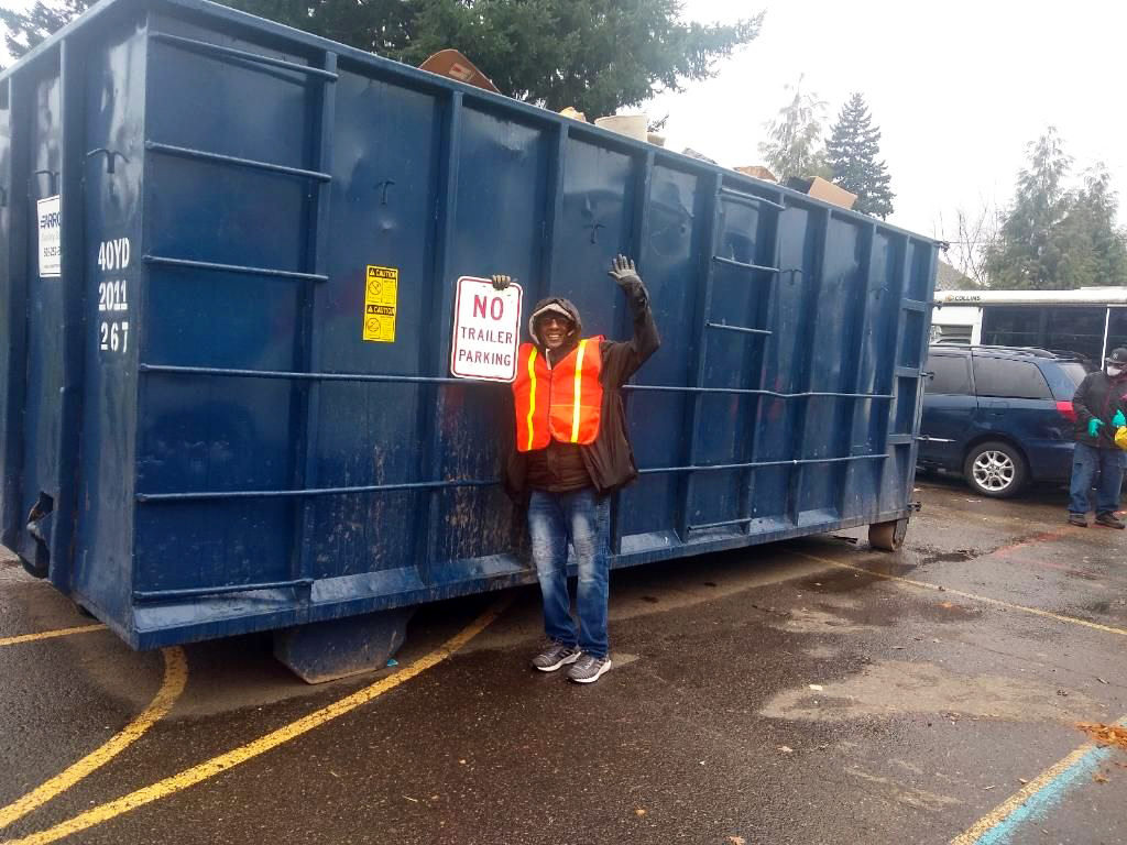 An image of a man in front of a large blue dumpster.