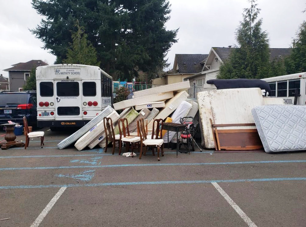 An image of a white bus next to a pile of mattresses and chairs.