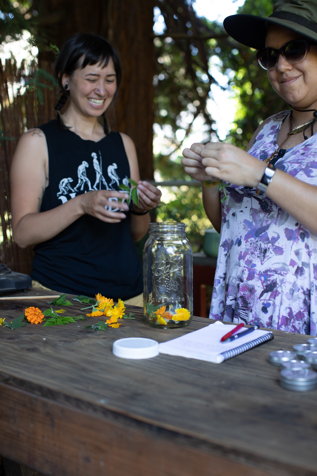 two people who are part of Atabey Medicine stand in front of a wooden table and place bright orange and yellow plants into a mason jar