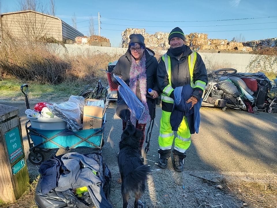 A woman, man and dog stand in front of a pile of trash along a multiuse pathway