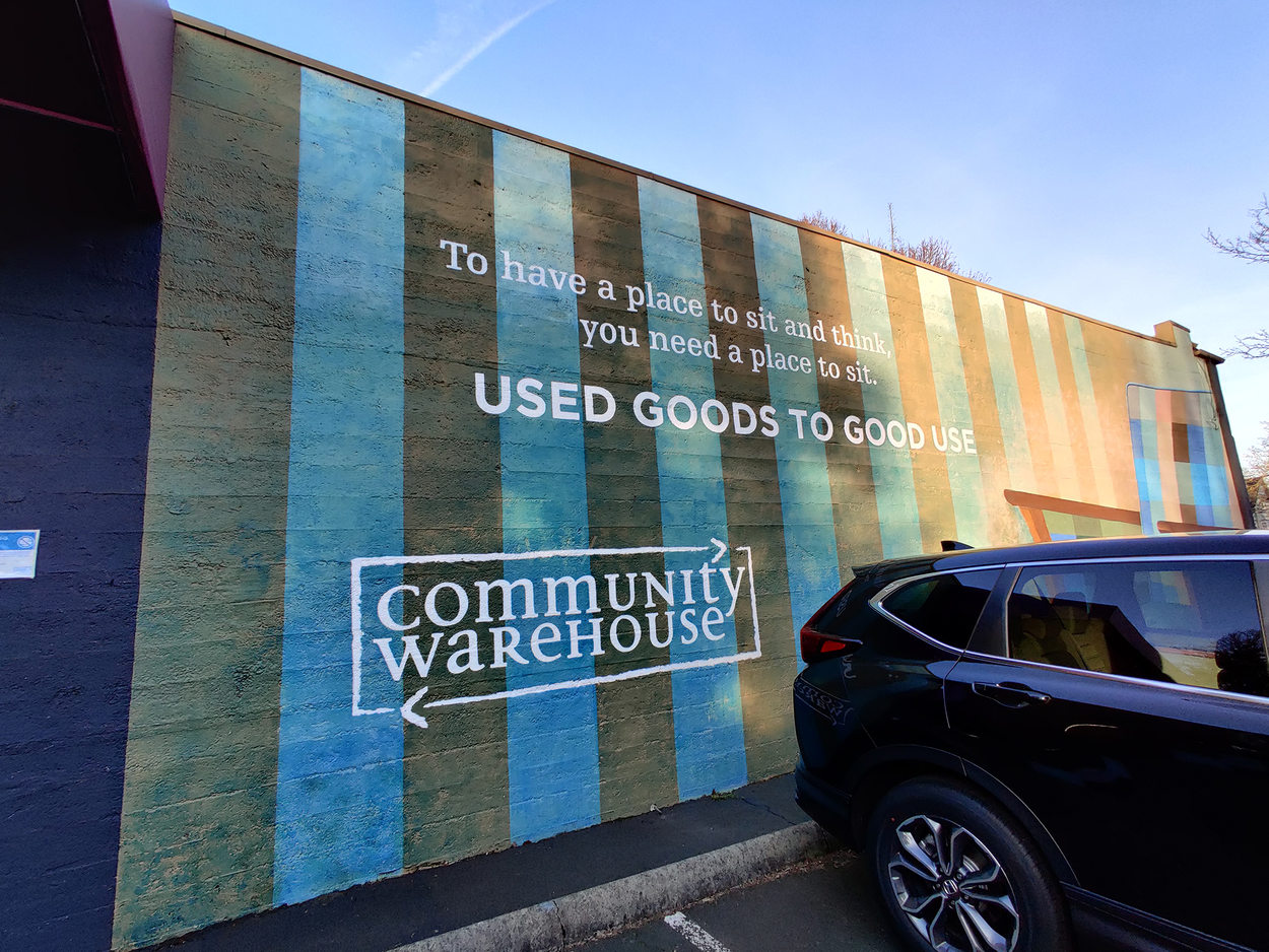 The side of a warehouse decorated in blue and green stripes, a slogan reads "used goods to good use"