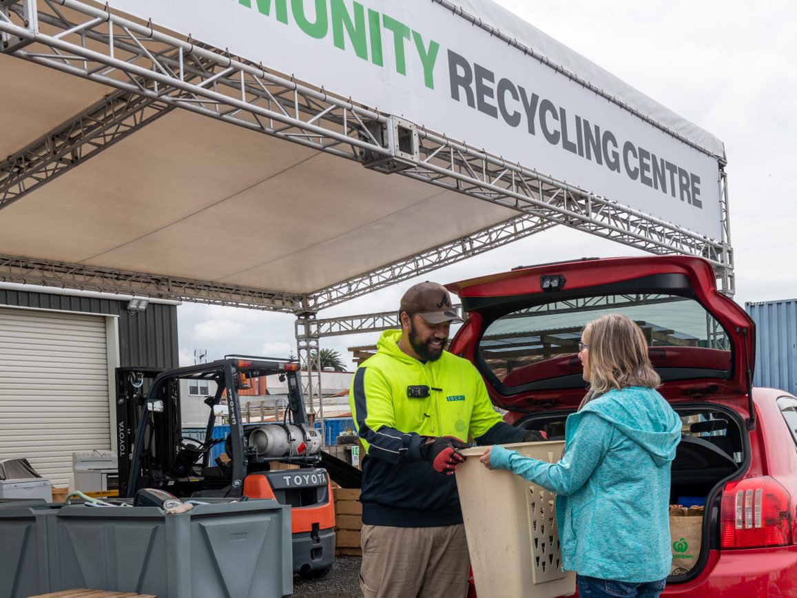 A person brings a basket of items to staff at a community recycling center