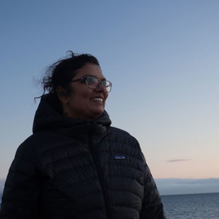 Raahi Reddy standing on a windy beach at dusk.