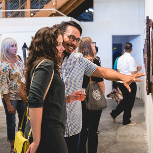 a smiling man enthusiastically takes about a piece of art to a woman next to him