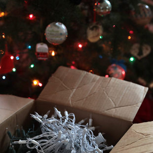 a box of string light sits in front of a Christmas tree