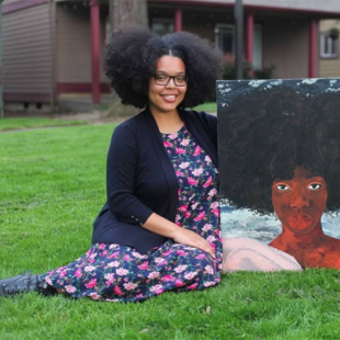  an artist sits on a grassy lawn while holding a painting she created