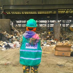 Artist in green safety vest stares at a giant pile of garbage