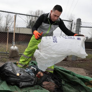 A man empties a large white trash bag onto the ground to sort through its contents