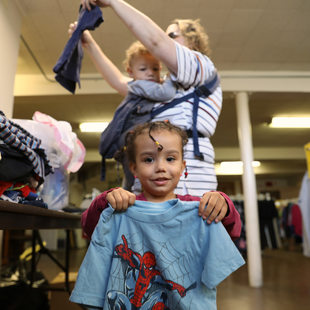 a little girl holds up a super hero shirt that she found in a clothing bin