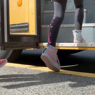 the feet of school children boarding a bus