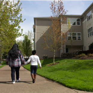 two people holding hands on the sidewalk near housing