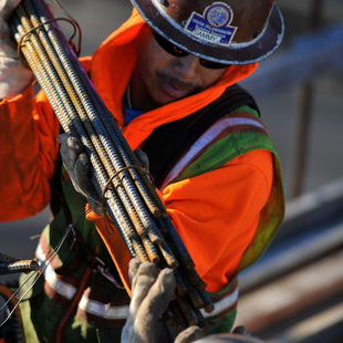 a construction worker carries a bundle of metal rebar at a construction site