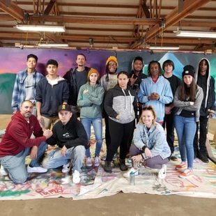 Young artists pose for a picture in front of a mural in progress