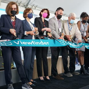 Nine people standing together cutting the ribbon with oversized scissors for the grand opening of Viewfinder apartments in Tigard