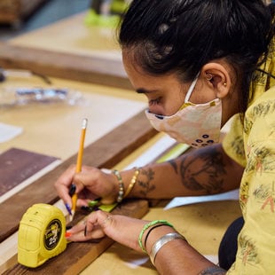 An image of a woman marking a measurement on a piece of wood.