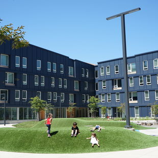 Children playing on a grass mound in front of dark blue multifamily housing