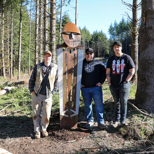 Three artists stand next to a statue at a park.