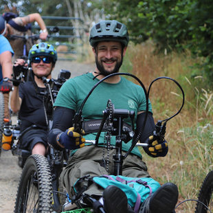 three adaptive mountain bikers, smiling, riding down a gravel path