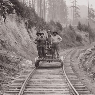 sepia-tone historical photo of Chinese railroad workers standing on a handcar on a railroad through woods, with one white worker in the middle of them