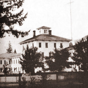 old monochrome photo of Oregon Hospital for the Insane surrounded by trees and a wooden fence