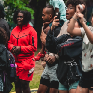 A crowd of mostly youth stand by, take videos and cheer on a live performance at George Park in the St. Johns neighborhood in Portland, Oregon