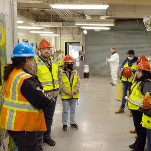 Group in safety vests and hardhats stand in a hallway of a hazardous waste disposal facility