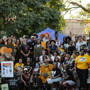 A crowd of mostly Black and brown people of all ages pose for a group photo at the Afro-topia pop-up event on stage.
