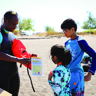 A swimming instructor shows two young children how to use a life vest 