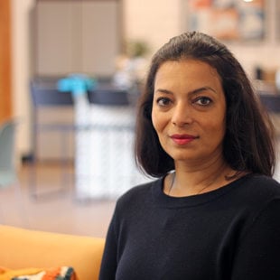 Woman with black hair and shirt looking at the camera, sitting in an indoor space