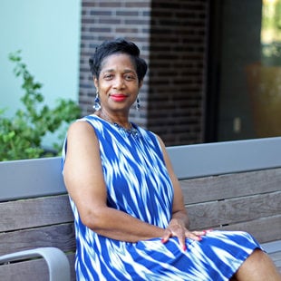 Woman with short dark hair and a blue print dress sitting on a bench