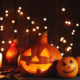 I small carved pumpkin is center, flanked by lit candles and oranges with faces painted on them.